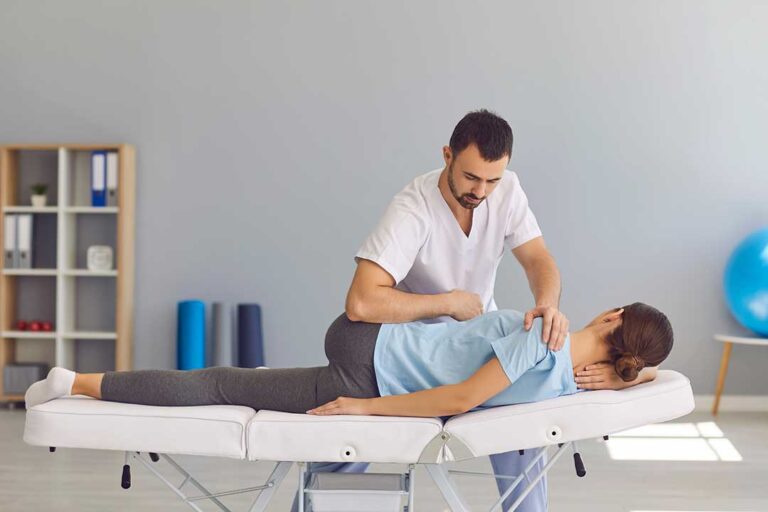 Person performing guided back exercises on a therapy mat beside a spine anatomy chart.