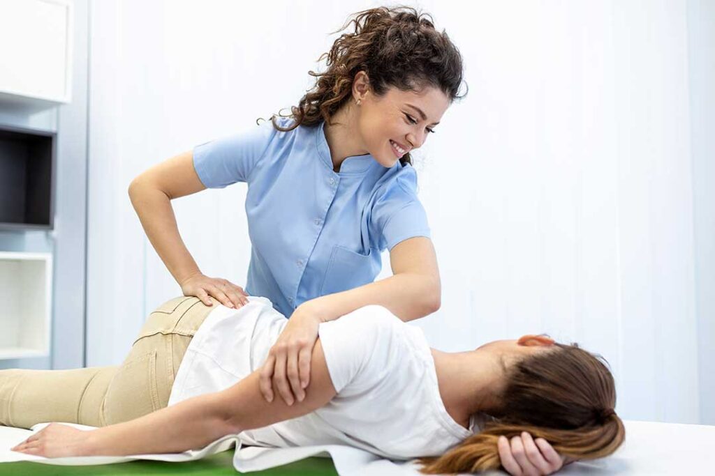 An adult rests on a living room couch with a heating pad on their lower back, gently stretching to ease discomfort.